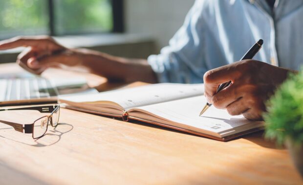 small business owner writing plans on a ledger from their laptop