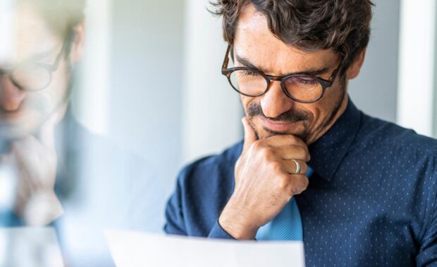 business man wearing glasses looking through a document by a window