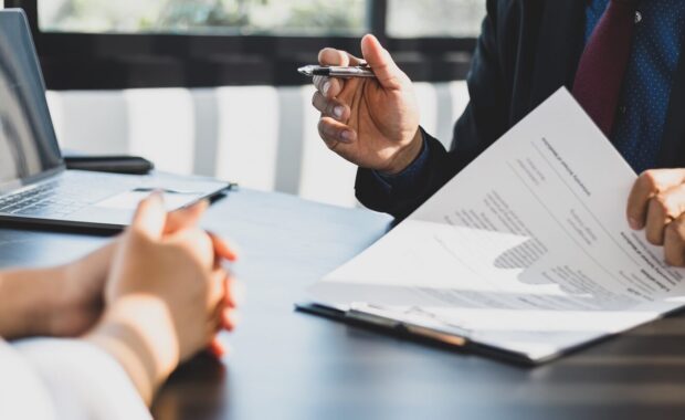 businessman in suit in his office showing an insurance policy and pointing with a pen where the policyholder must to sign